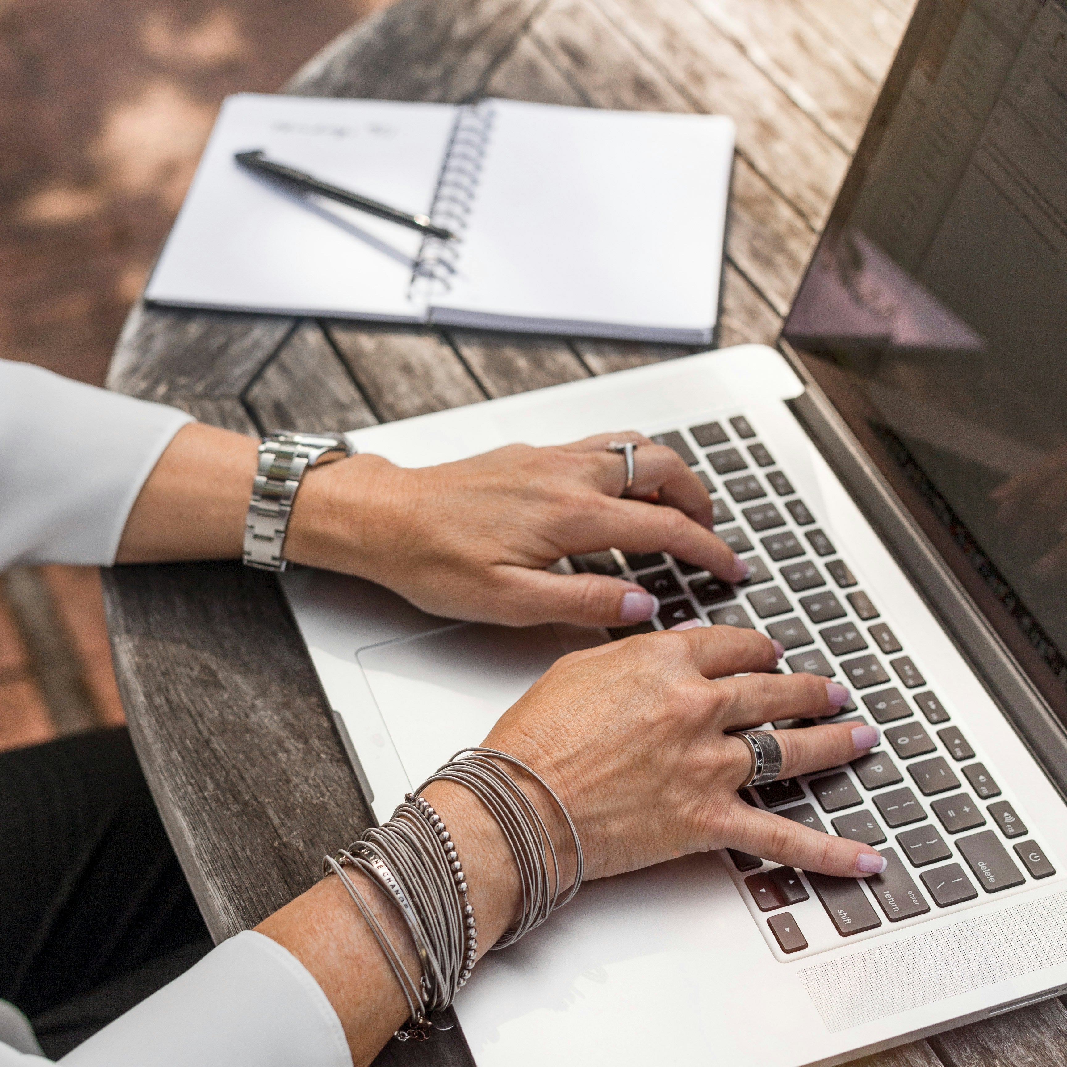 Woman typing on a laptop outside on wooden table.
