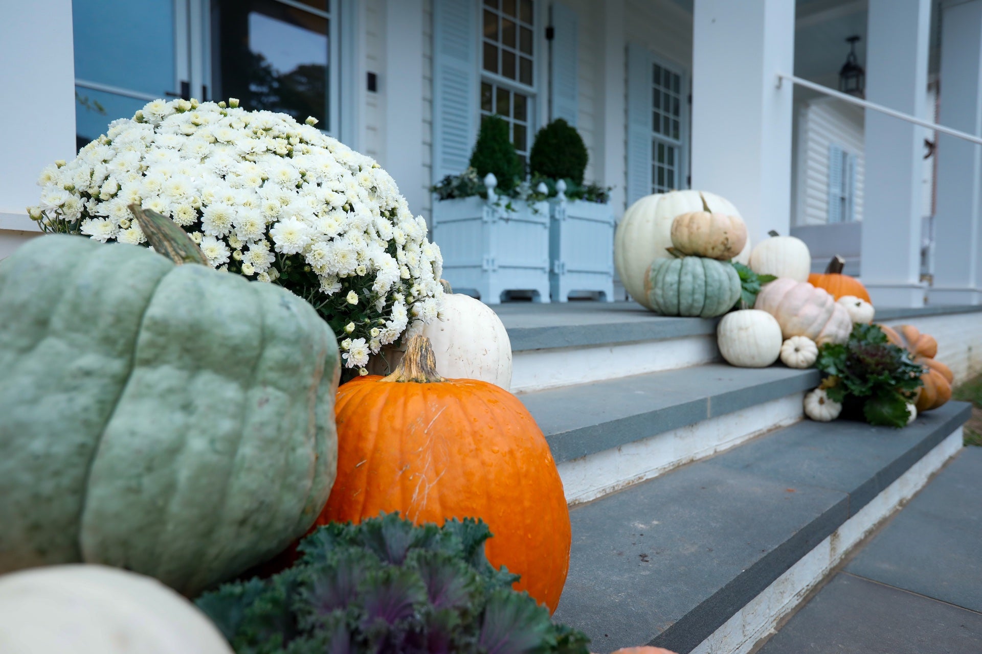 Decorative pumpkins and flowers on a front porch with a house in the background