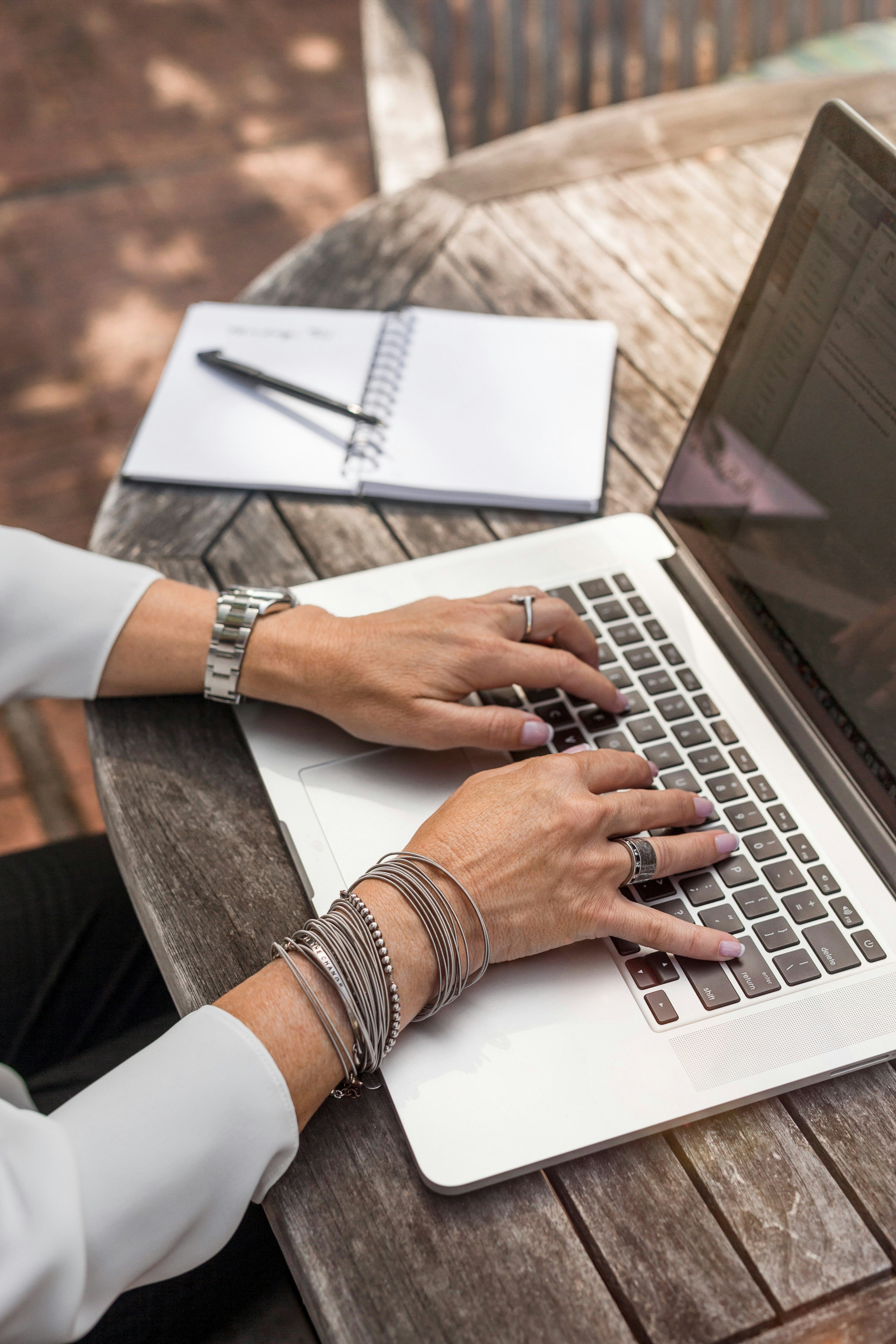 Woman typing on a laptop outside on wooden table.
